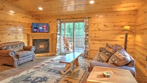 A cozy cabin interior with a fireplace, leather sofas, a wooden coffee table, and a television mounted on the wall. - Blessings Lodge (Millersburg)