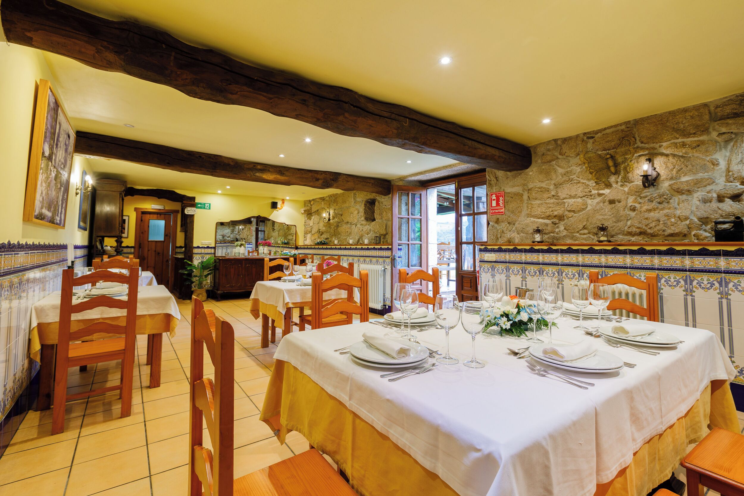 A dining area with tables set for a meal, wooden chairs, and a stone wall.