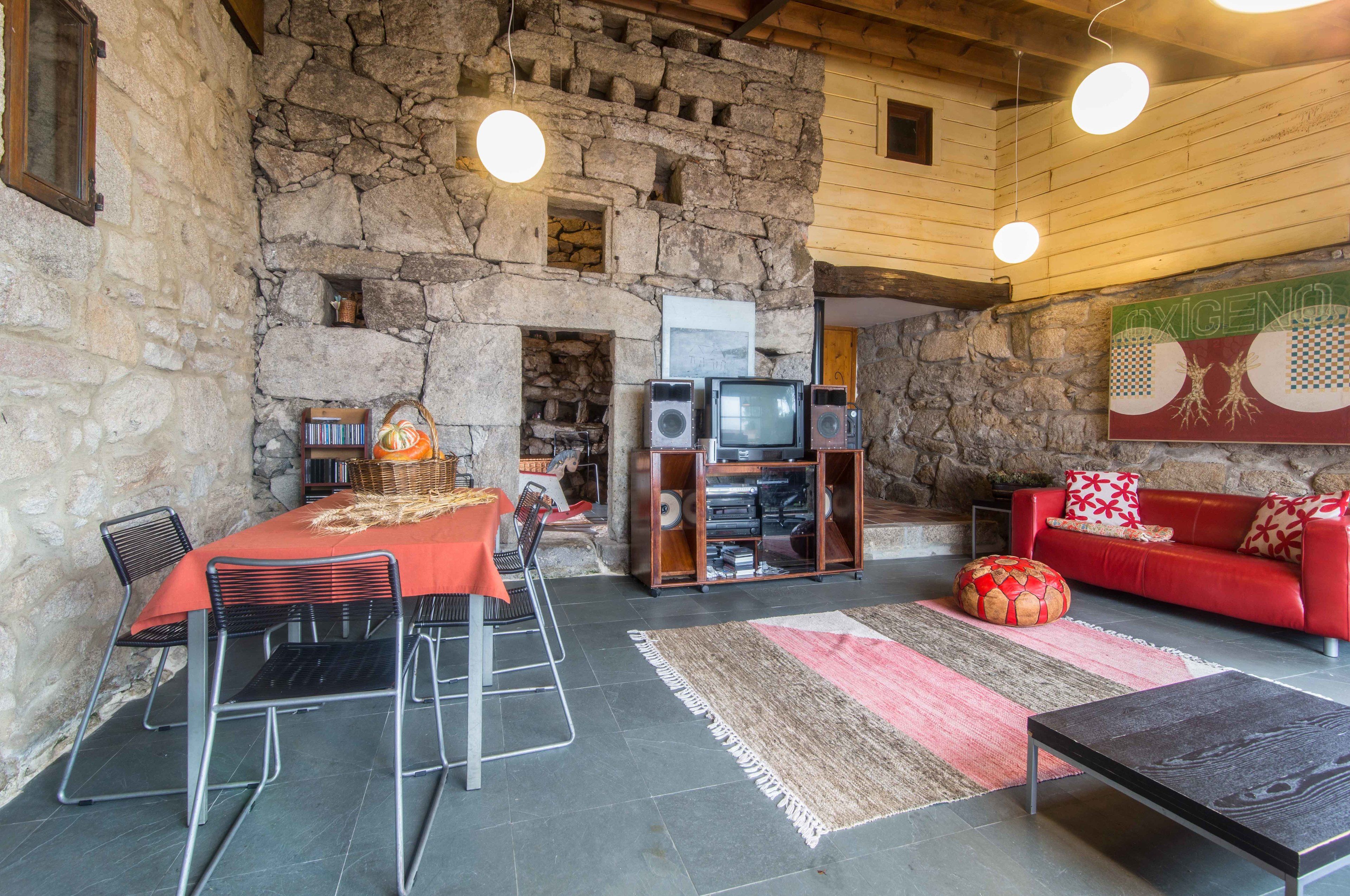 A rustic stone interior with a dining area, a red sofa, and a television set.