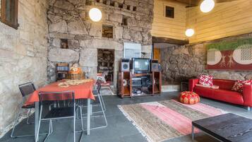 Un interno rustico in pietra con zona pranzo, un divano rosso e un televisore.