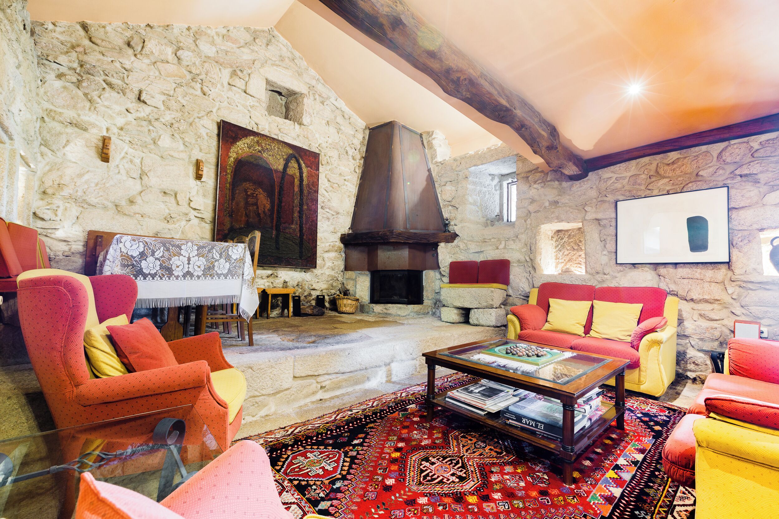 Un salón acogedor con paredes de piedra, chimenea y asientos coloridos.