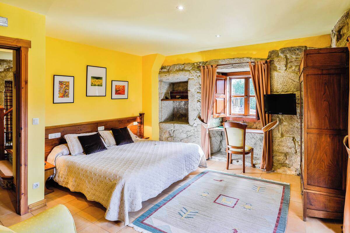 A bedroom with a bed, a desk, a chair, and a stone wall.