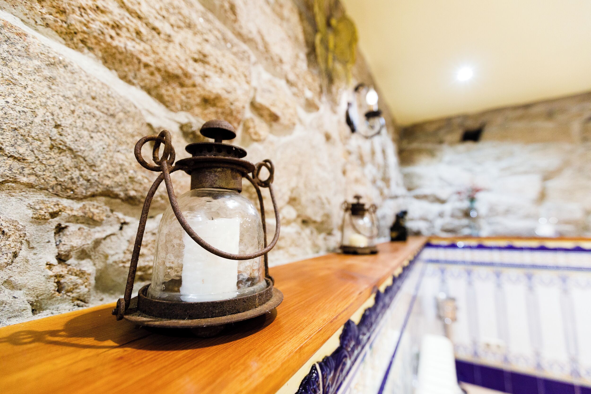 A rustic stone wall with a wooden shelf holding a lantern and a candle.