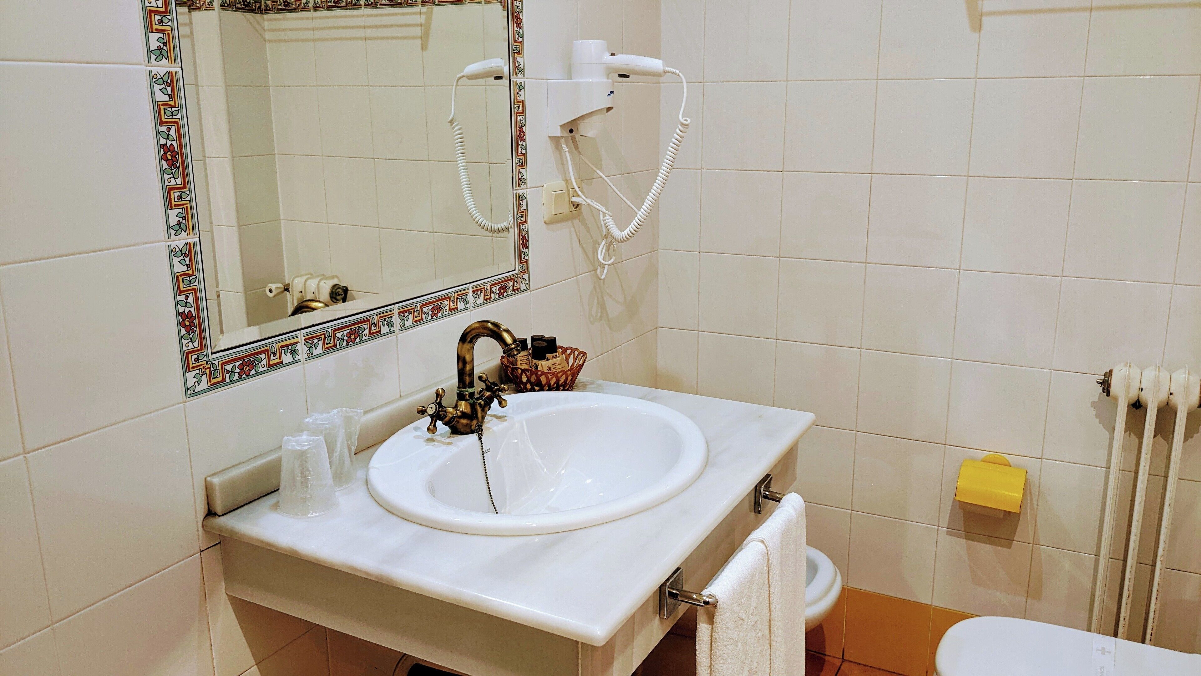 Un bagno con un lavandino bianco, uno specchio con cornice decorativa, un asciugacapelli e un water.