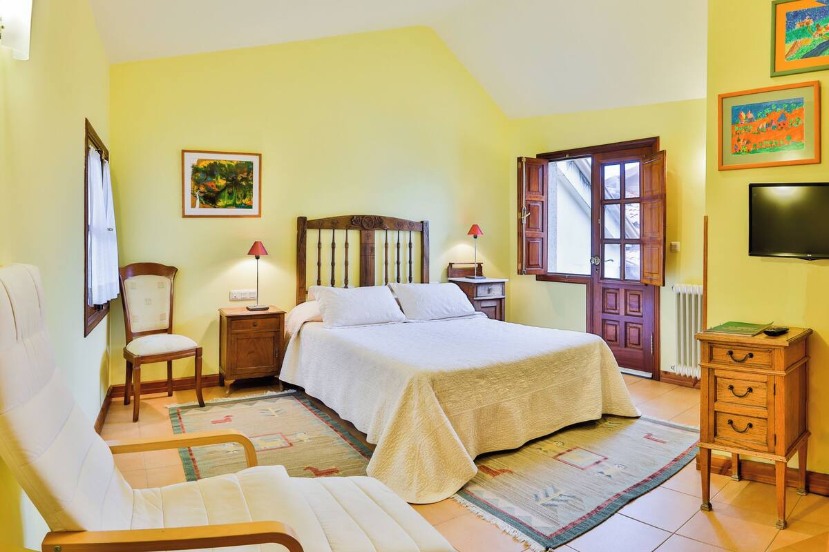 A bedroom with a bed, two chairs, a nightstand, a lamp, a dresser, and a TV.