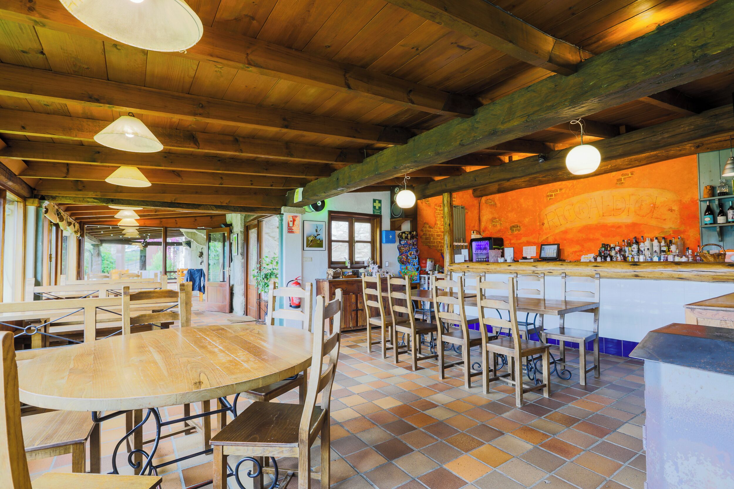 Ein Restaurant mit Holztischen und -stühlen, einer Bar und einem gefliesten Boden.
