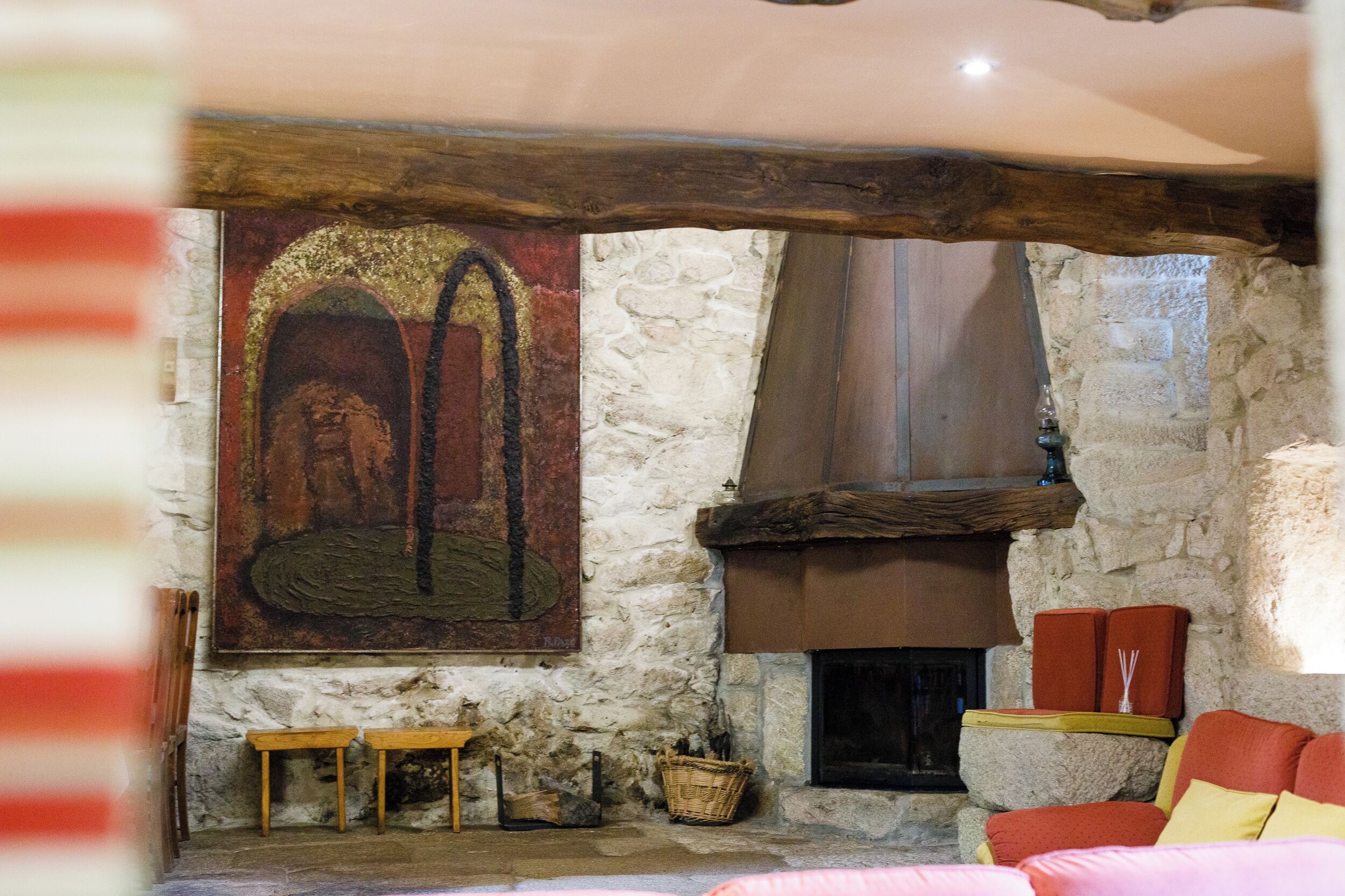 Un intérieur rustique avec des murs en pierre, une cheminée, des bancs en bois et un tableau aux couleurs vives.