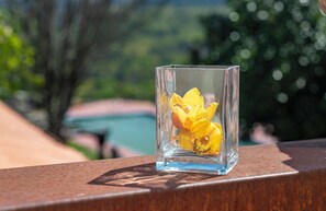 Un florero de vidrio transparente con flores amarillas sobre una barandilla metálica.