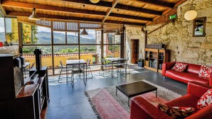 A spacious living area with a stone wall, a red leather sofa, a dining table with chairs, and a view of mountains through large windows. - Rectoral de Fofe (Covelo)