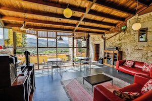 Un salón amplio con pared de piedra, un sofá de cuero rojo, una mesa de comedor con sillas y vistas a montañas a través de grandes ventanales.