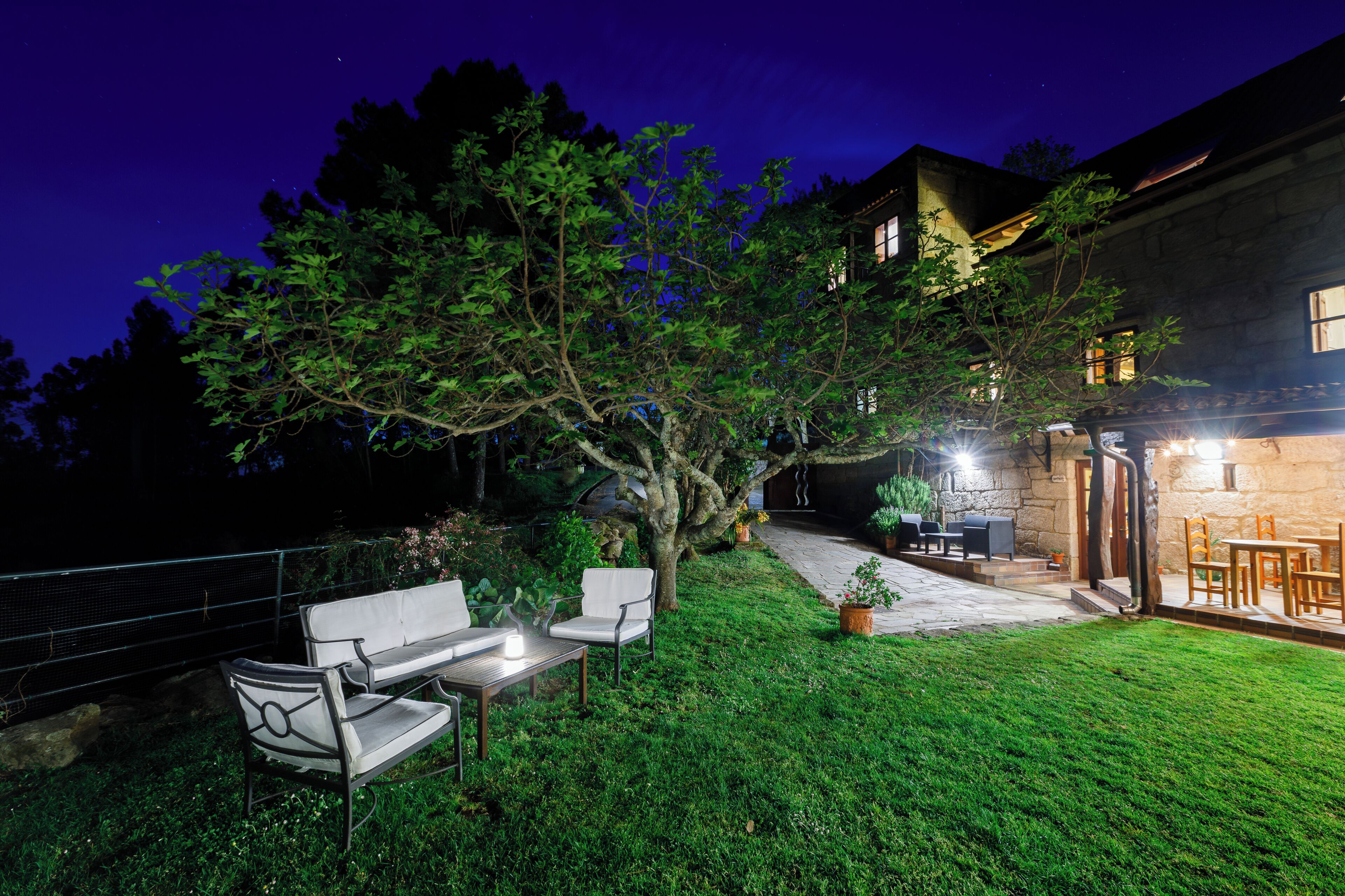 An outdoor patio area with a stone wall, a tree, and a seating arrangement including a table and chairs.