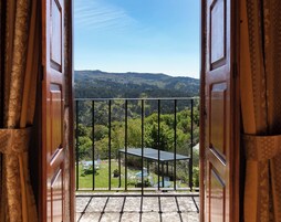 Un balcón abierto con vistas a un paisaje verde y una mesa con sillas.
