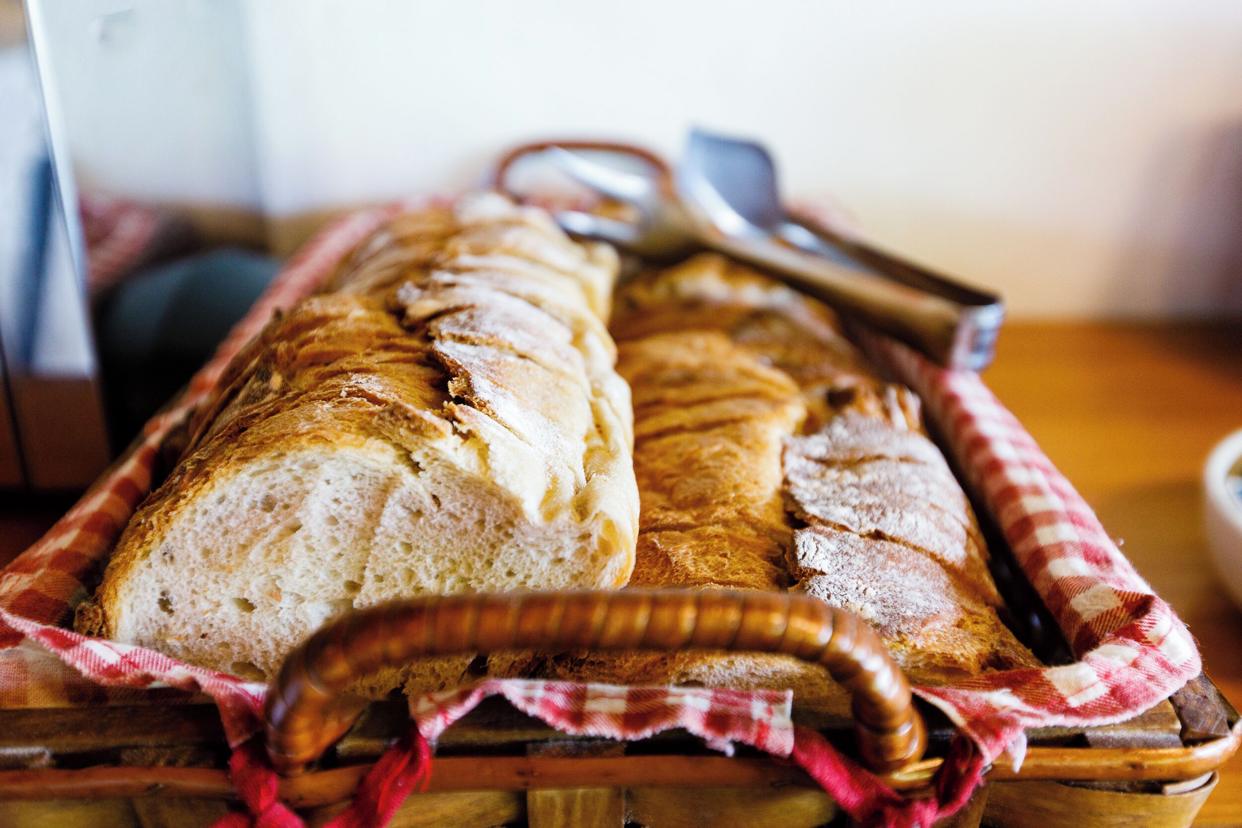 A loaf of bread in a wooden basket with a checkered cloth.