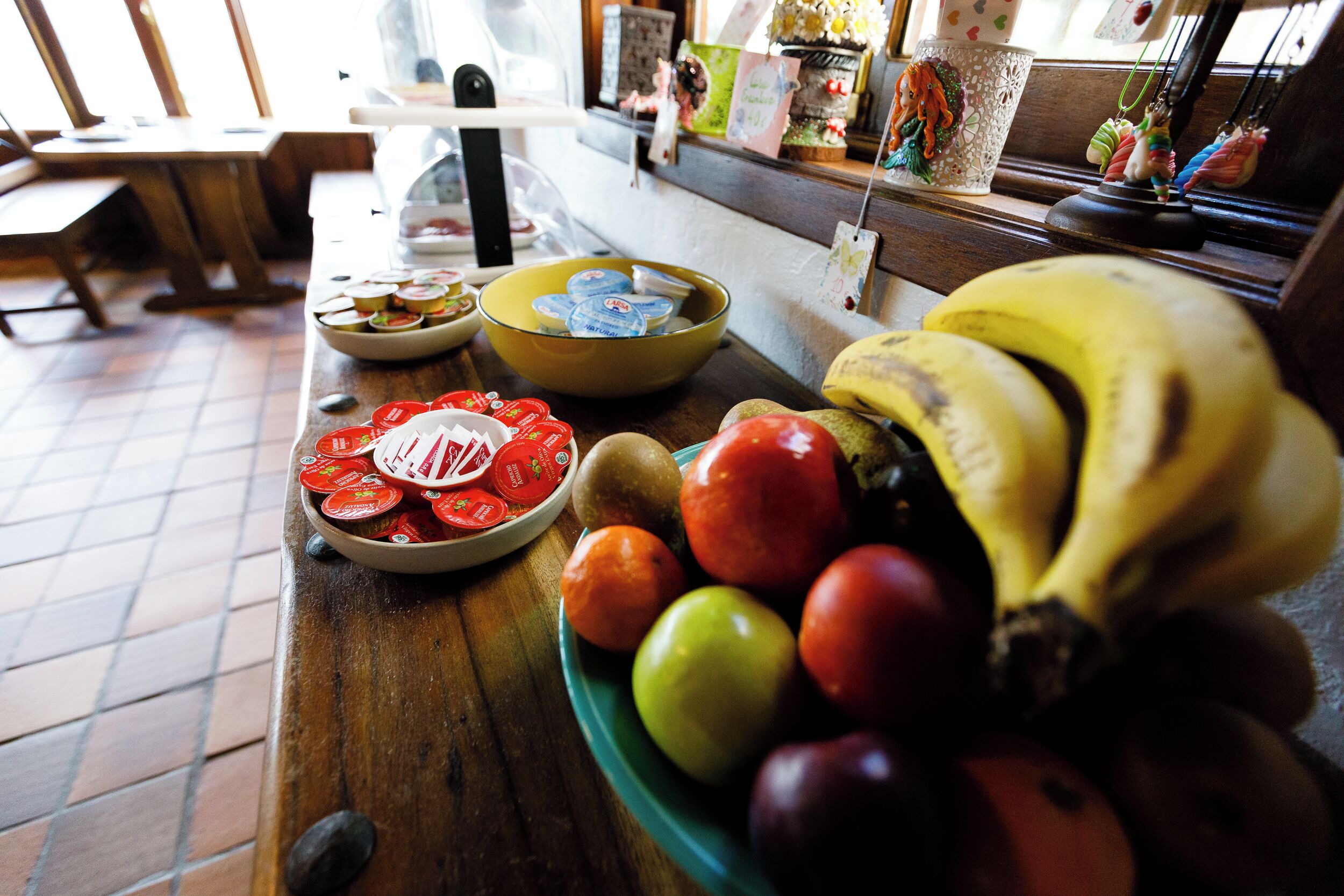 A table with a bowl of yogurt, a plate of sliced tomatoes, and a bowl of mixed fruits including bananas and apples.