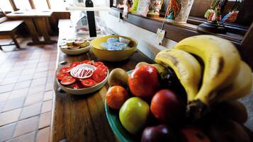 A table with a bowl of yogurt, a plate of sliced tomatoes, and a bowl of mixed fruits including bananas and apples.