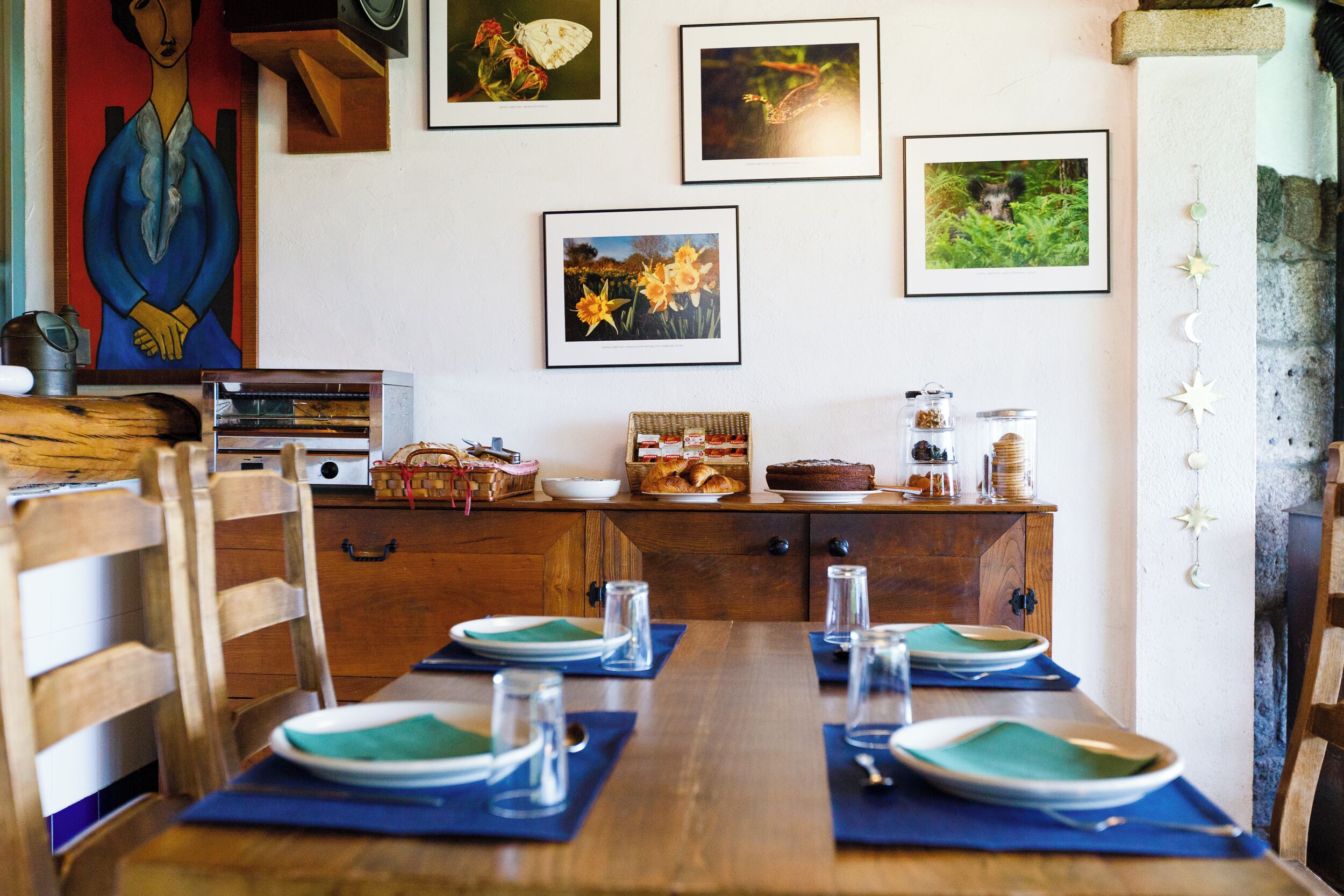 Un comedor con una mesa de madera dispuesta para cuatro, una obra de arte en la pared y una chimenea de piedra.