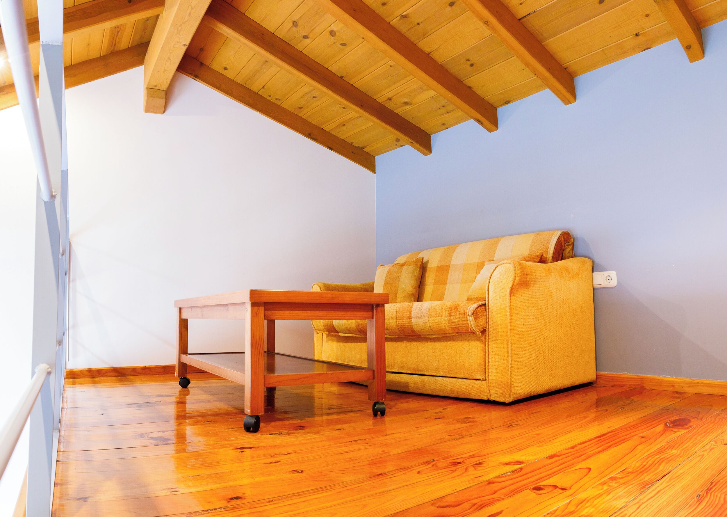 Una habitación con piso de madera, un sofá amarillo y una pequeña mesa de madera.