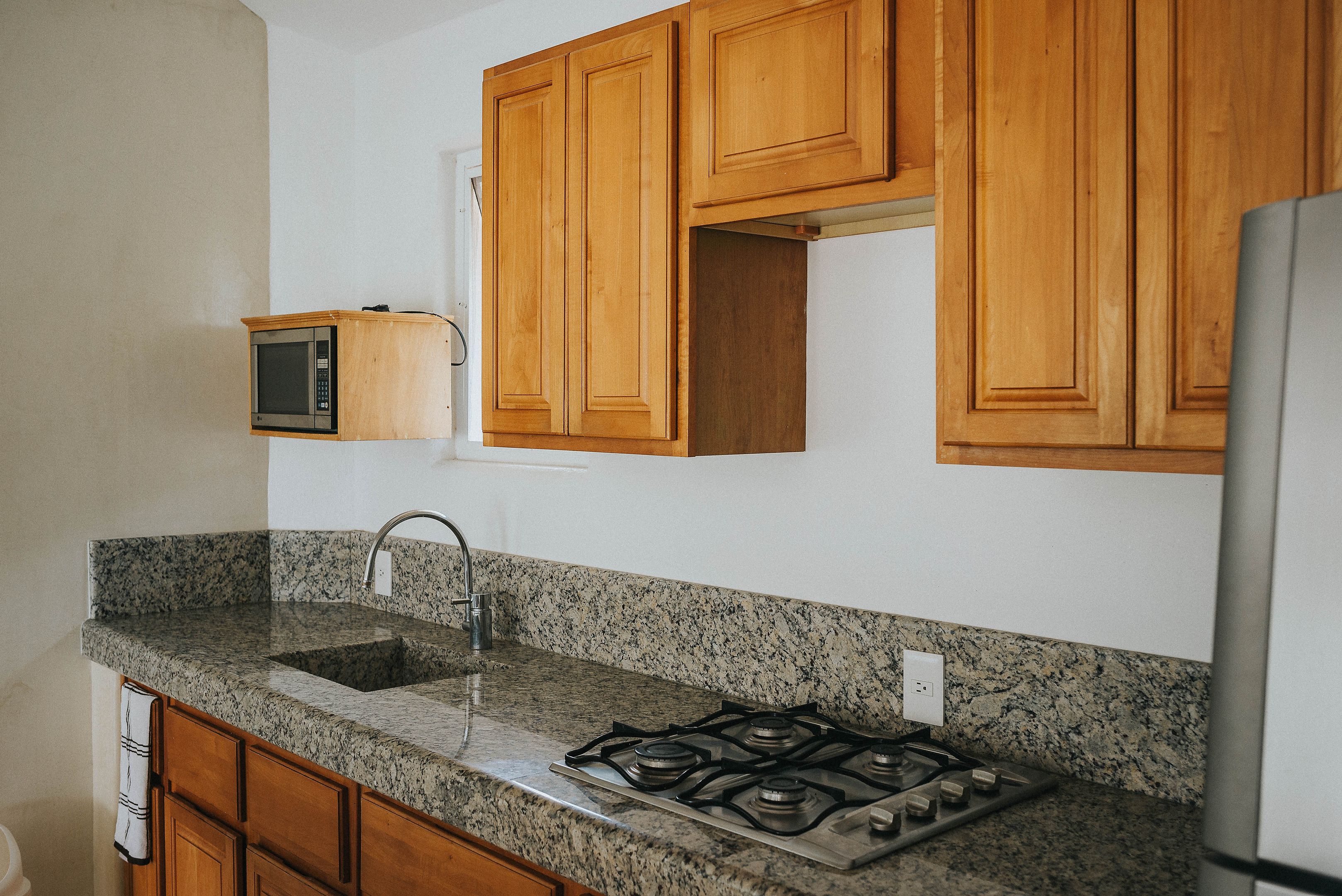 Una cocina con encimeras de granito, armarios de madera, microondas integrado, estufa a gas y refrigerador de acero inoxidable.