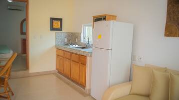 Una cocina compacta con armarios de madera, un refrigerador blanco y una zona de comedor con una silla de mimbre.
