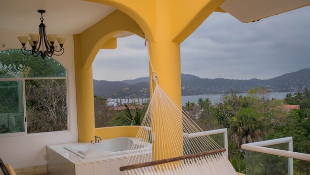 A balcony with a hammock, a bathtub, and a view of a lake and mountains.