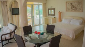 A hotel room with a bed, a glass table with chairs, a TV mounted on the wall, and a balcony with curtains.