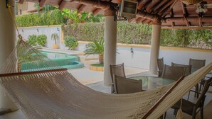 A hammock in a covered outdoor area with a pool and patio furniture.