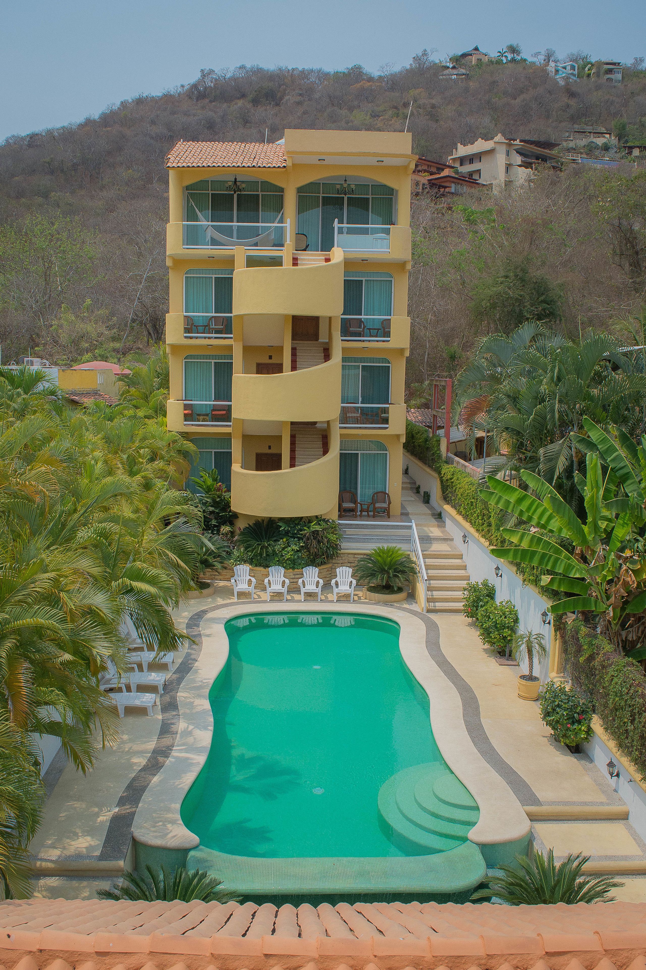 A multi-story hotel with a pool, surrounded by palm trees and greenery.