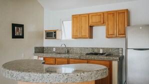 A kitchen with wooden cabinets, a granite countertop, a stainless steel refrigerator, and a microwave.