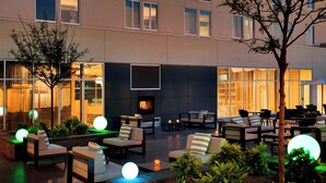 An outdoor seating area with multiple chairs and sofas, a fire pit, and illuminated spherical lights. - Aloft by Marriott Dallas Love Field (Dallas)