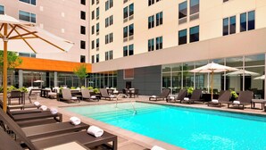 A hotel pool area with sun loungers, umbrellas, and a glass building in the background. - Aloft by Marriott Dallas Love Field (Dallas)