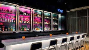 A bar area with multiple shelves of bottles, a long counter with bar stools, and a neon sign. - Aloft by Marriott Dallas Love Field (Dallas)
