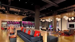 A modern lounge area with a sofa, ottomans, and a bar area with a neon sign. - Aloft by Marriott Dallas Love Field (Dallas)