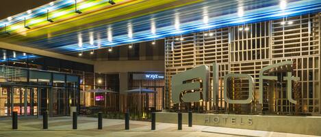 A hotel entrance with a modern design, featuring a large illuminated sign and a glass facade.
