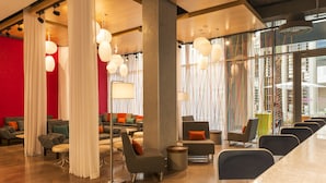 En moderne hotellobby med en rød accentvæg, siddeområder og store vinduer med udsigt over byen.