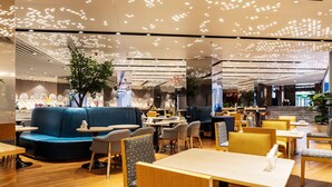 A modern restaurant with blue seating, wooden tables, and a ceiling with patterned lights.