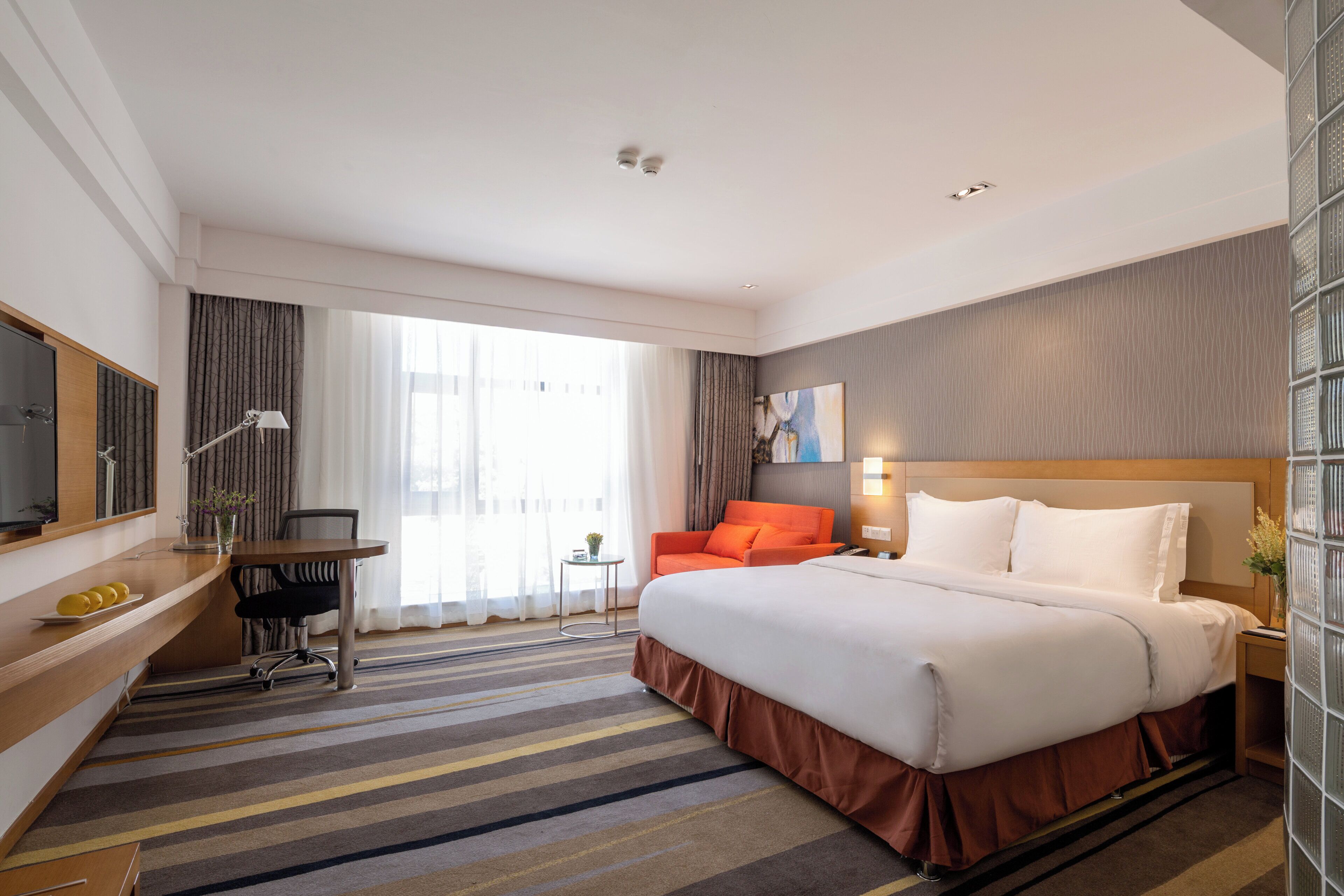 A hotel room with a bed, a desk, a chair, a TV, and a window with curtains.