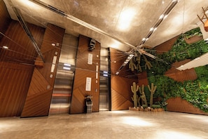 A modern elevator with a digital display, a wooden wall with a geometric pattern, and a green wall with plants. - Holiday Inn Express Daocheng Yading by IHG (Garze)