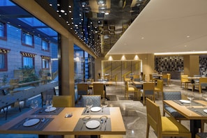 A modern restaurant with multiple dining tables, chairs, and a patterned wall in the background. - Holiday Inn Express Daocheng Yading by IHG (Garze)