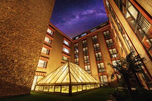 En byggnad med en pyramidformad konstruktion av glas i mitten, omgiven av murade väggar och flera fönster.