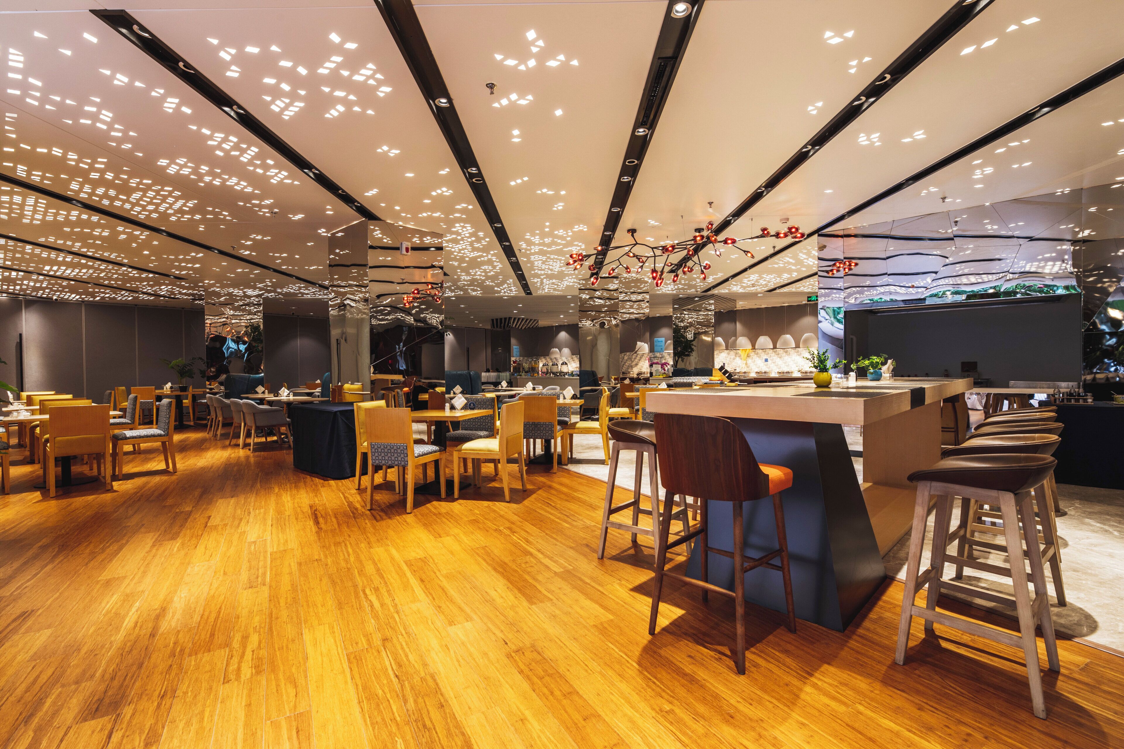 A modern restaurant interior with wooden flooring, multiple seating areas, and a central bar.