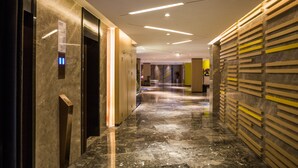 A modern hotel corridor with marble flooring, elevators, and a wooden wall with horizontal slats.