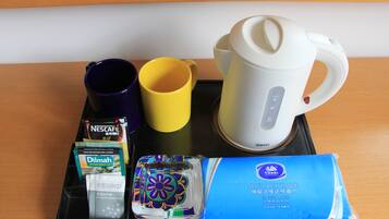 A tray with a white electric kettle, a purple and a yellow mug, a Nescafe coffee packet, a Dilmah tea packet, a pack of Vinda tissue, and a decorative item.