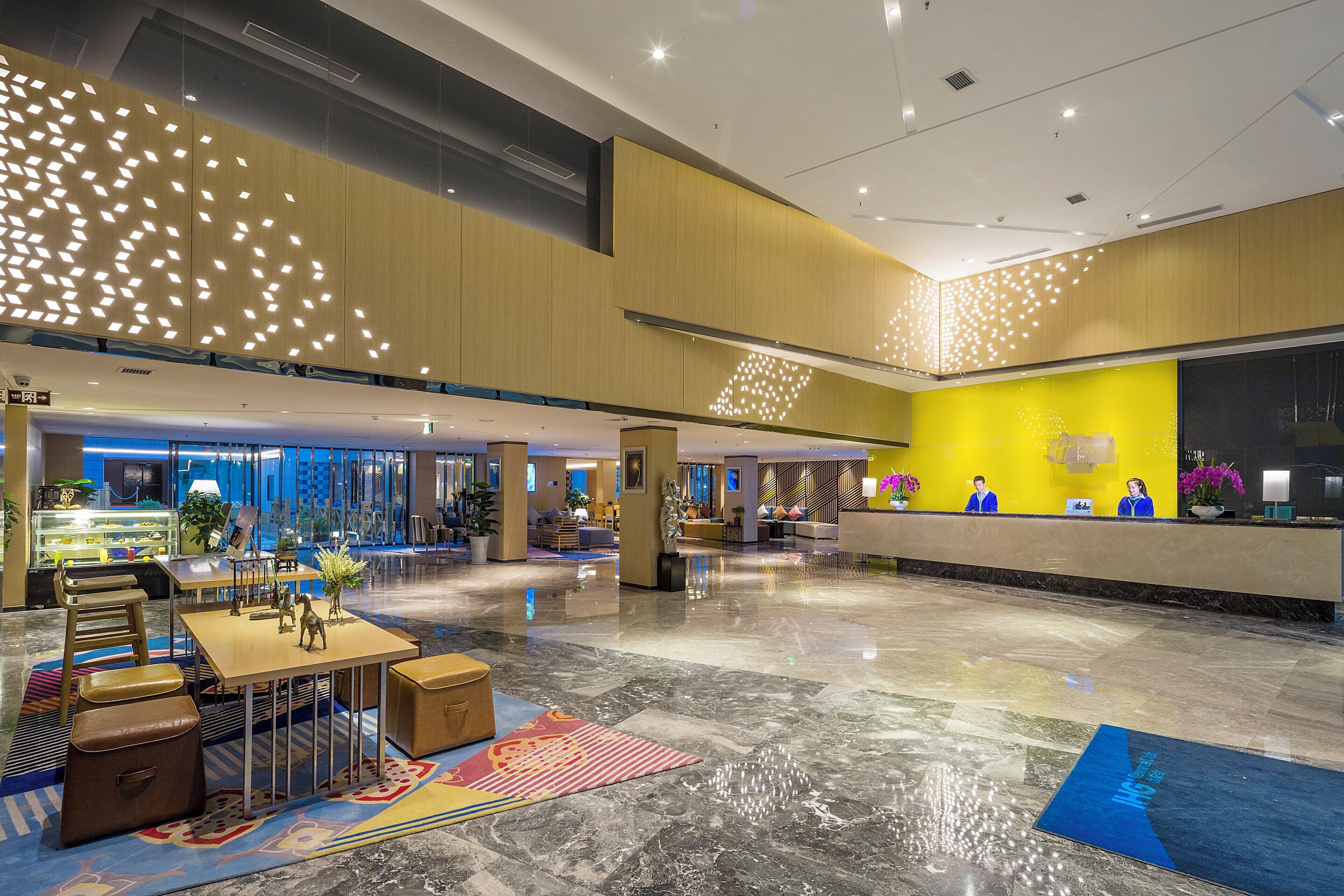A spacious lobby with a reception desk, seating area, and a glass wall offering a view of the outside.