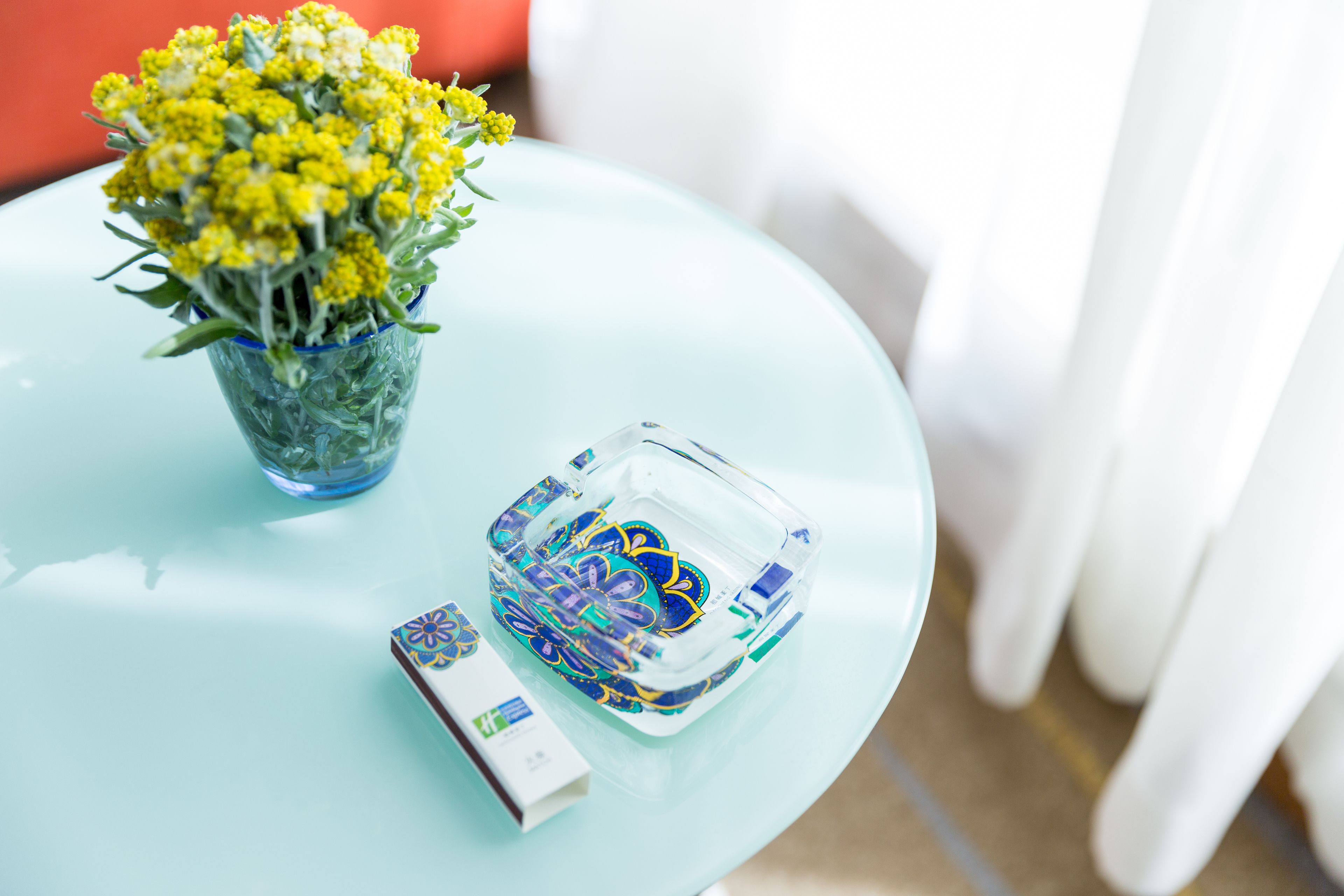A glass table with a vase of yellow flowers, a decorative box, and a small container.