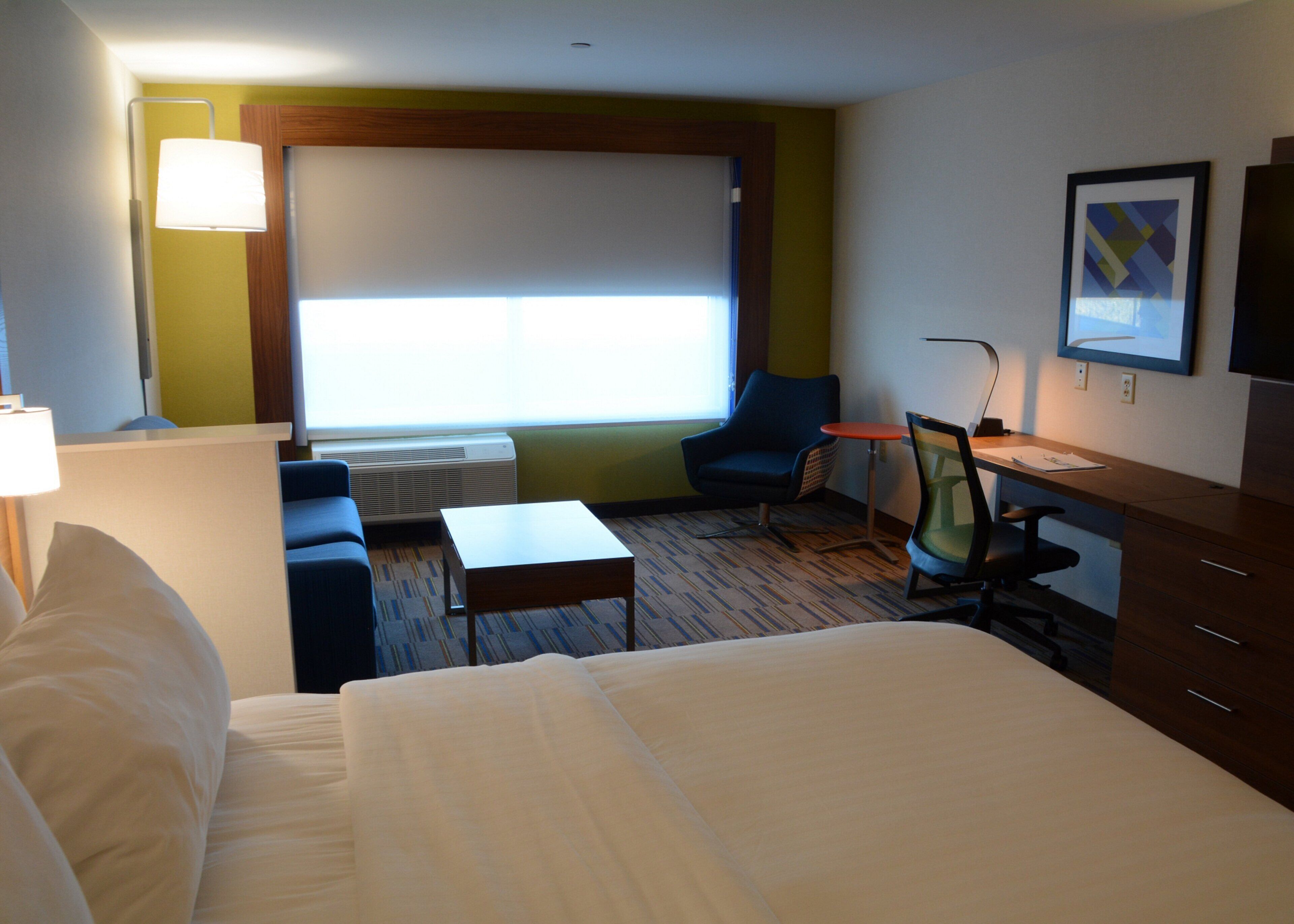 Una habitación de hotel con cama, escritorio, silla, sofá y ventana.