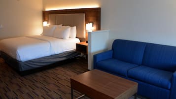Une chambre d’hôtel avec un lit, un canapé bleu, une table basse en bois et une table de chevet avec une lampe.