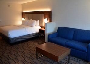 A hotel room with a bed, a blue sofa, a wooden coffee table, and a nightstand with a lamp.