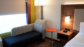 A hotel room with a sofa, a small table, a bedside table with a lamp, and a bed.