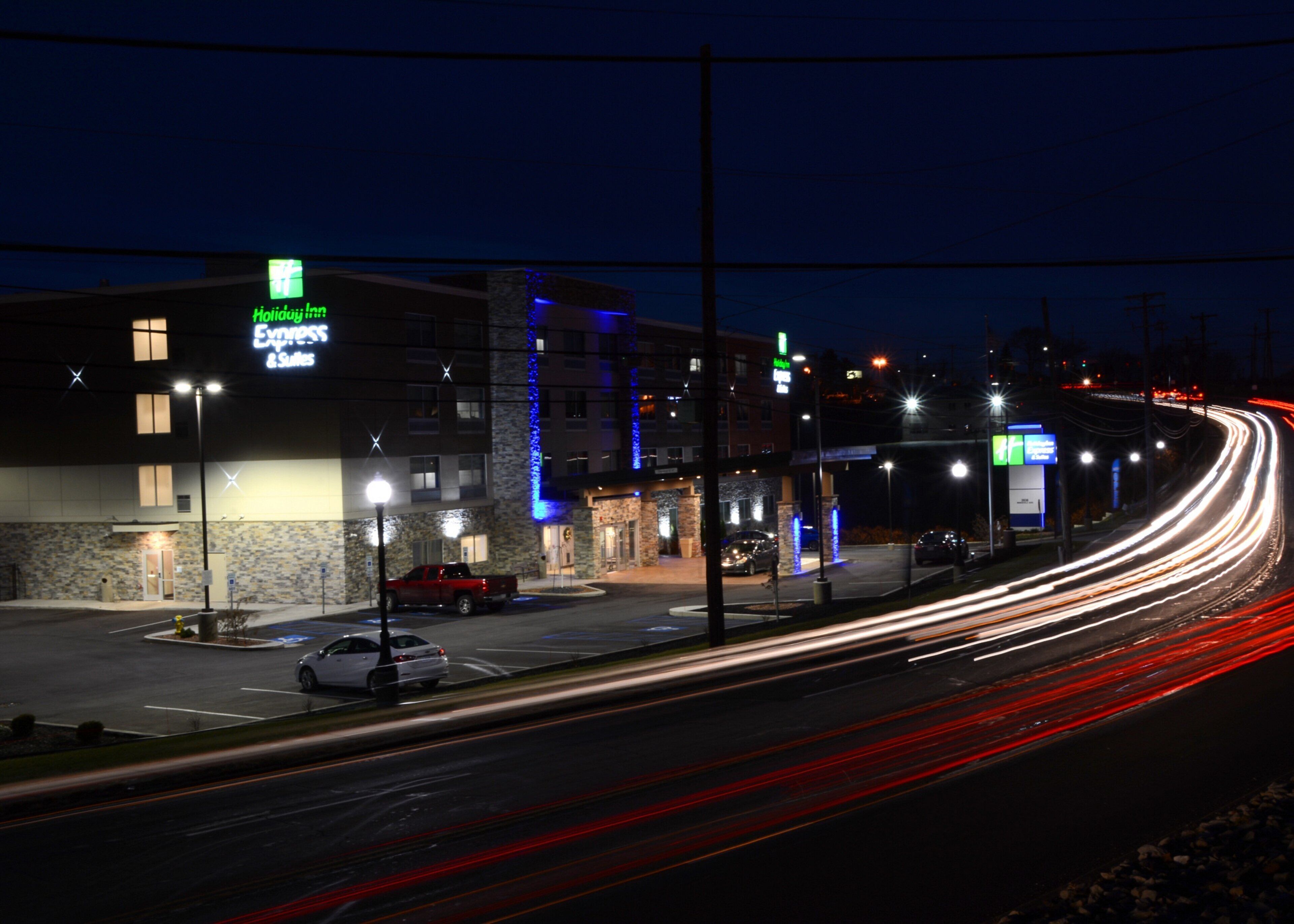 A Holiday Inn Express & Suites with a stone facade, a parking lot, and a road with light trails indicating traffic.