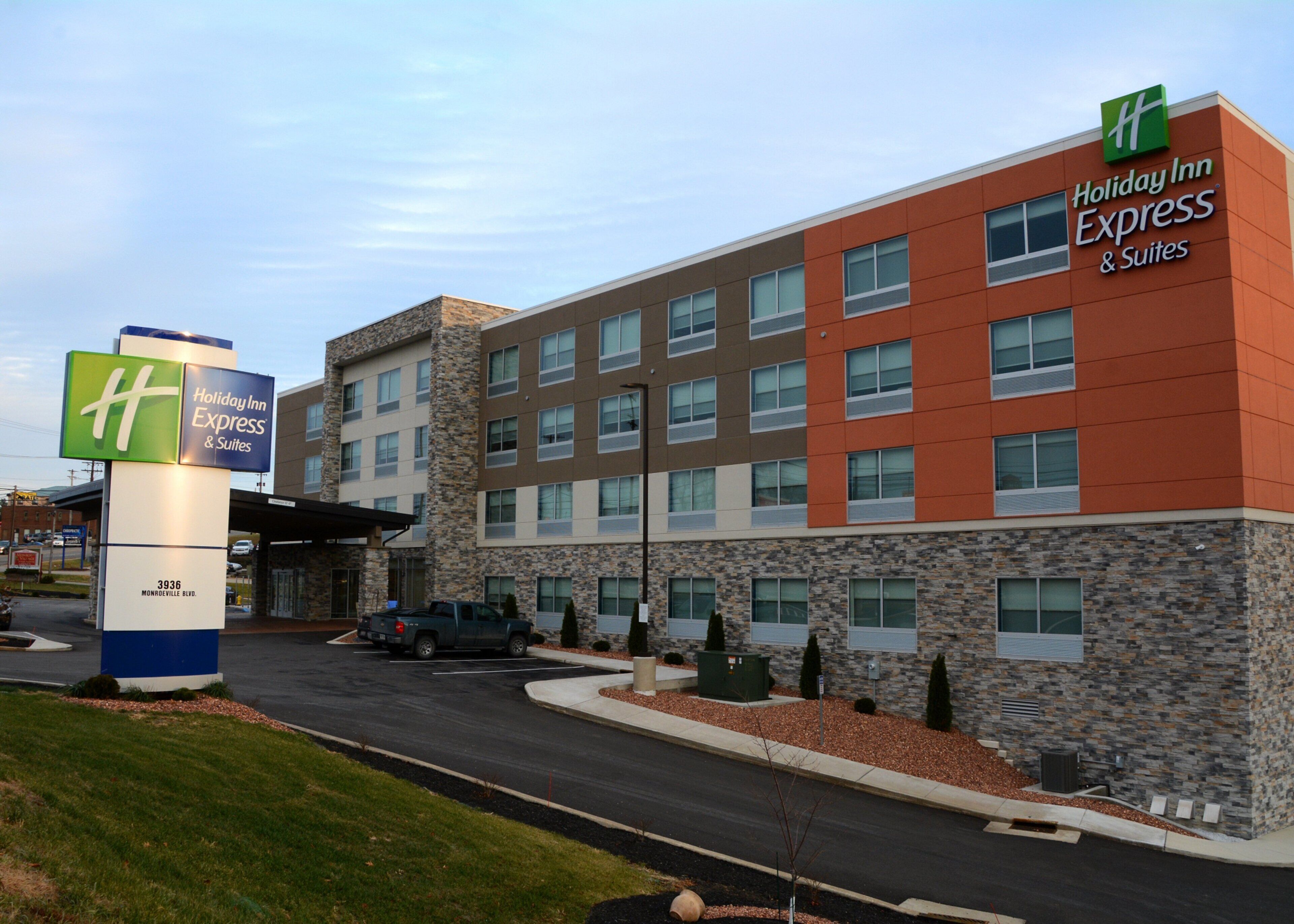Edificio de Holiday Inn Express & Suites con fachada de piedra, múltiples ventanas y un estacionamiento.